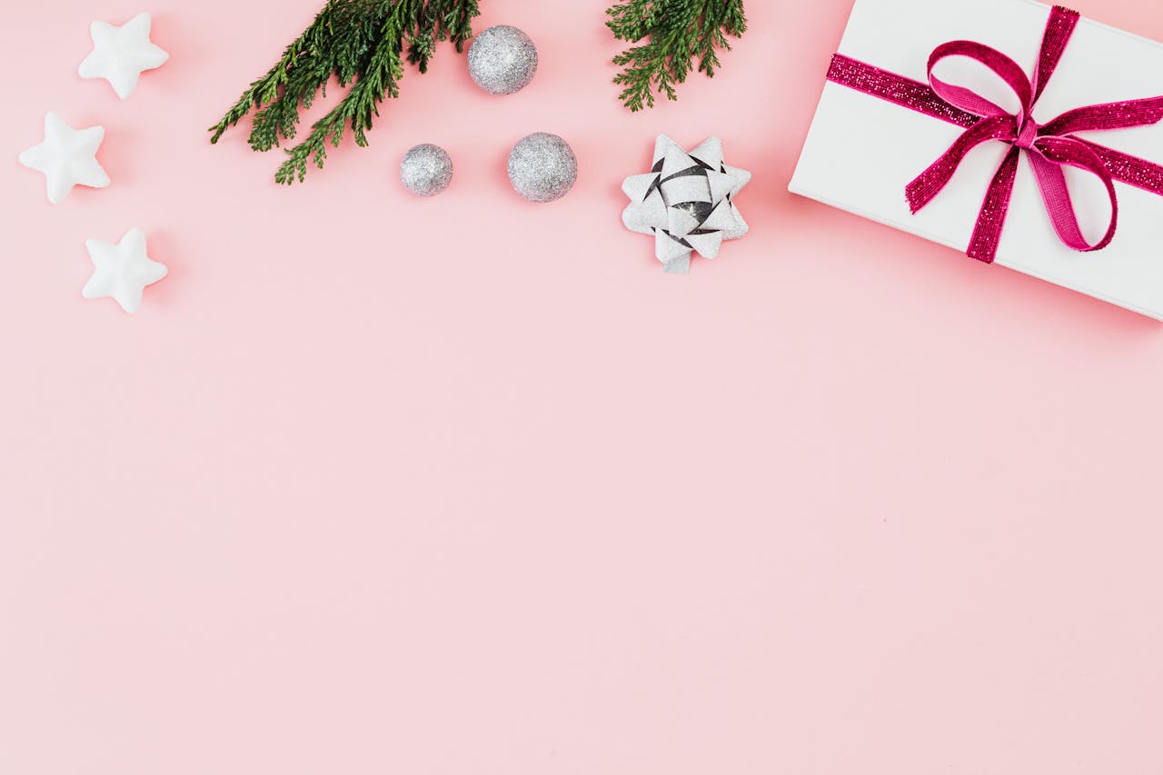 Festive flat lay with gift, stars, and ornaments on pink pastel background, ideal for holiday greetings.